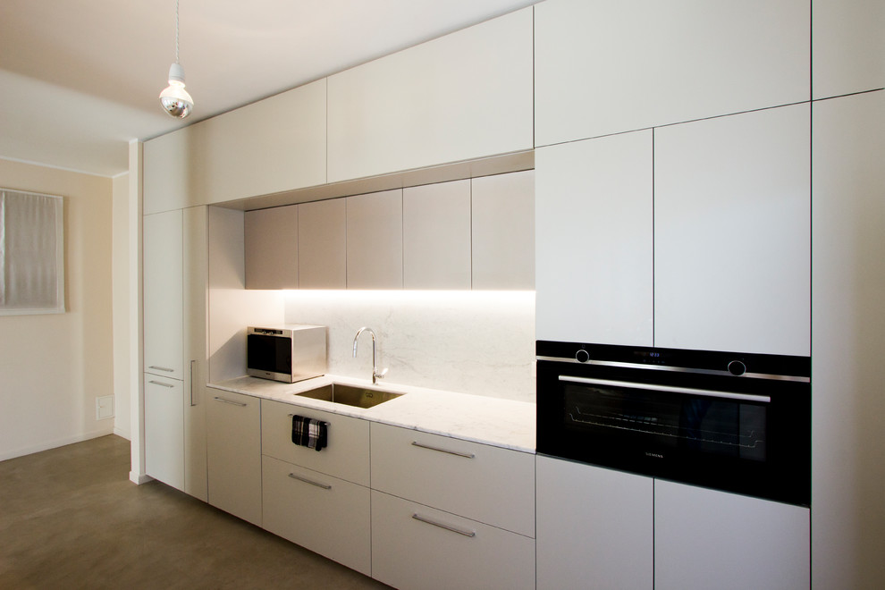 Photo of a large contemporary galley eat-in kitchen in Milan with an undermount sink, flat-panel cabinets, grey cabinets, marble benchtops, white splashback, marble splashback, black appliances, concrete floors, with island, grey floor and white benchtop.