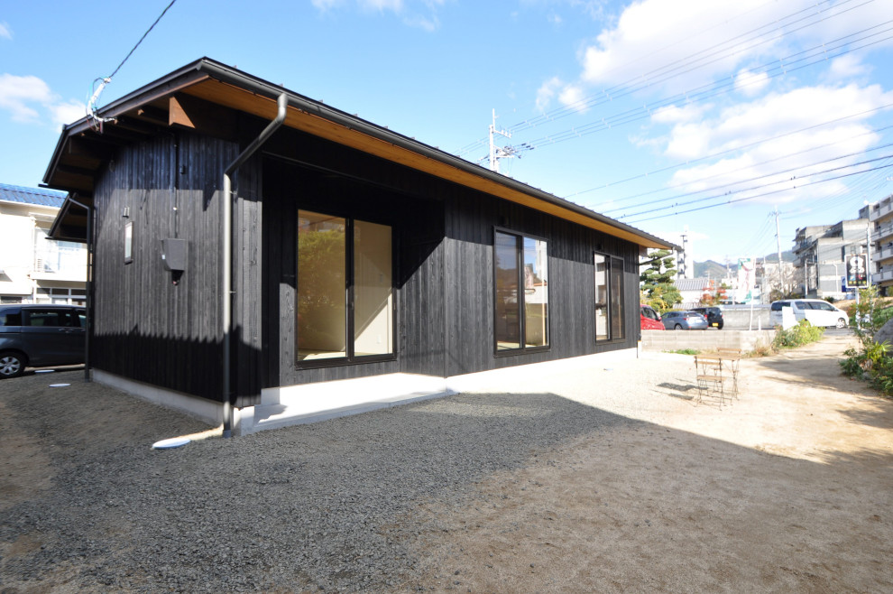 Small one-storey black house exterior in Other with wood siding, a gable roof, a metal roof, a blue roof and board and batten siding.
