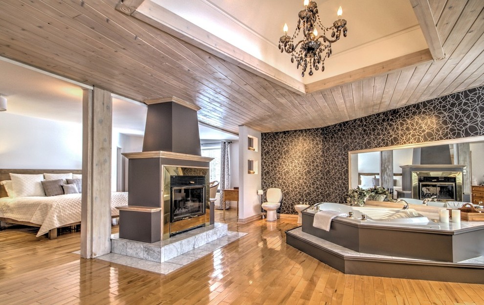 Expansive traditional master bedroom in Montreal with black walls, light hardwood floors, a two-sided fireplace and a metal fireplace surround.