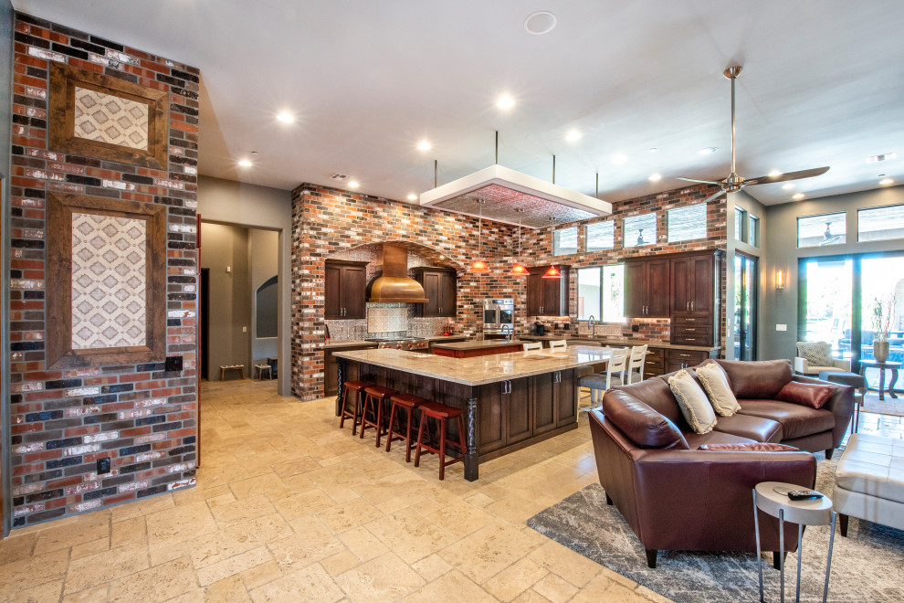 Inspiration for an expansive arts and crafts l-shaped open plan kitchen in Phoenix with a farmhouse sink, shaker cabinets, brown cabinets, granite benchtops, metallic splashback, metal splashback, stainless steel appliances, travertine floors, multiple islands, beige floor and red benchtop.