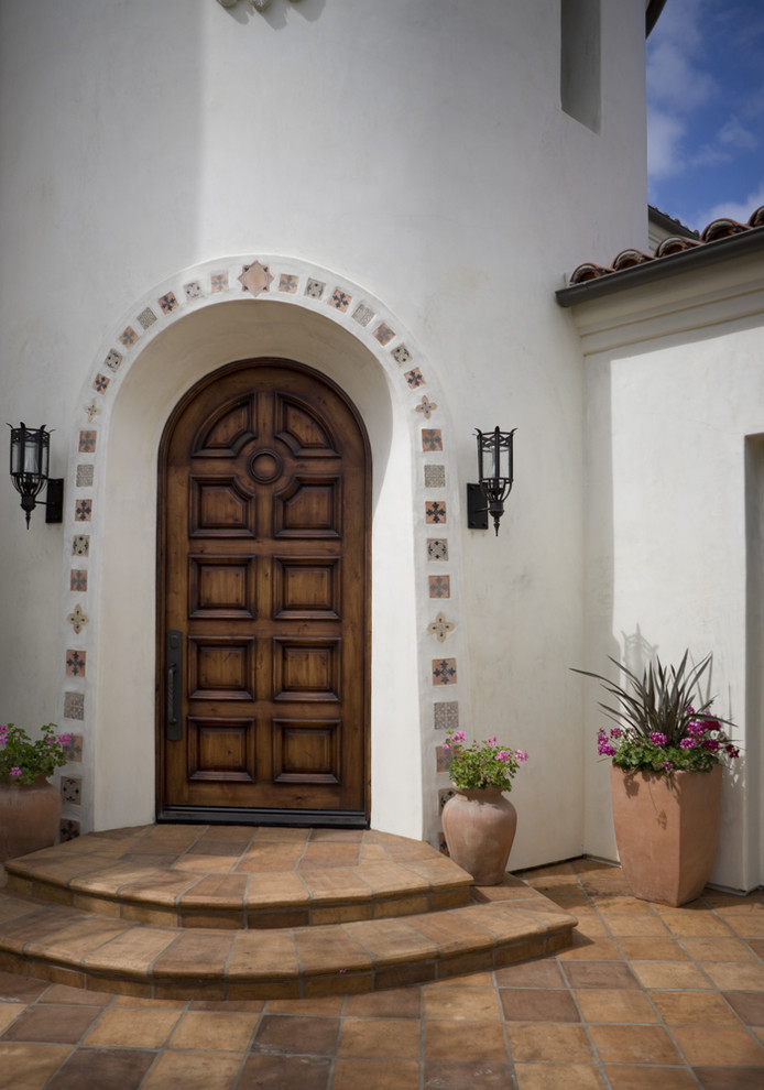 Mediterranean front door in Orange County with terra-cotta floors, a single front door and a dark wood front door.