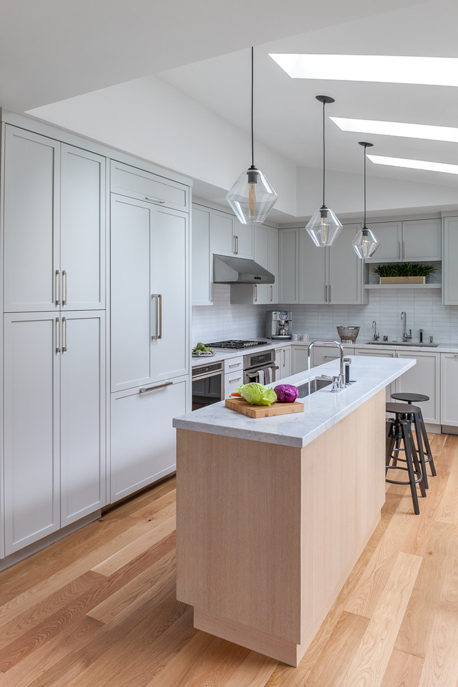 Mid-sized transitional galley eat-in kitchen in San Francisco with a drop-in sink, recessed-panel cabinets, grey cabinets, marble benchtops, grey splashback, ceramic splashback, panelled appliances, light hardwood floors and with island.