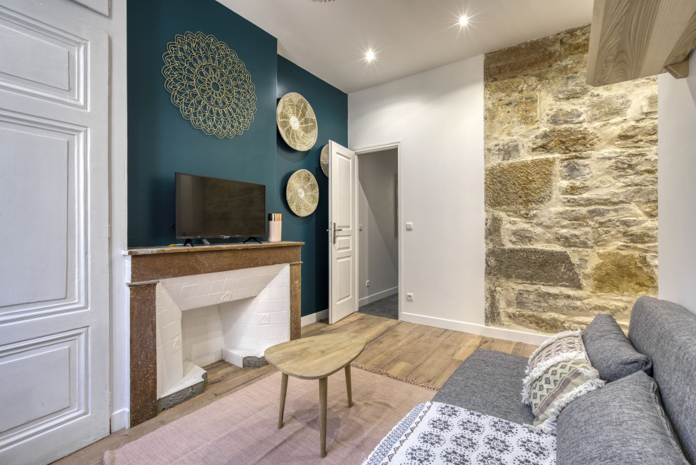 Cette image montre un petit salon nordique ouvert avec un mur vert, un sol en bois brun, une cheminée standard, un manteau de cheminée en pierre de parement et un téléviseur indépendant.