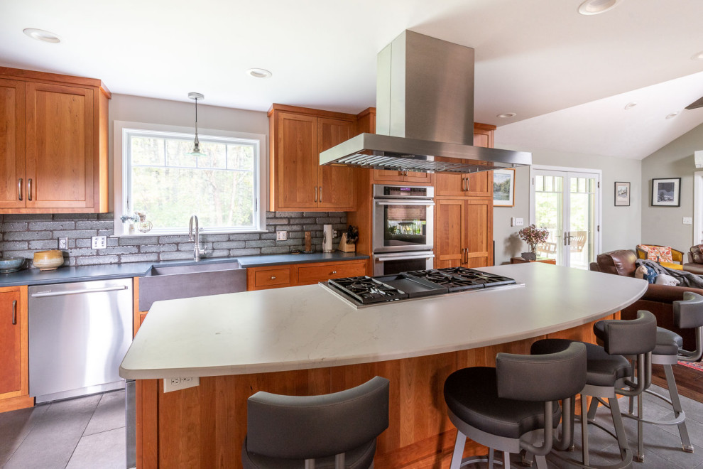 Inspiration for a large transitional l-shaped porcelain tile and gray floor eat-in kitchen remodel in Boston with a farmhouse sink, shaker cabinets, medium tone wood cabinets, quartz countertops, gray backsplash, porcelain backsplash, stainless steel appliances, an island and white countertops