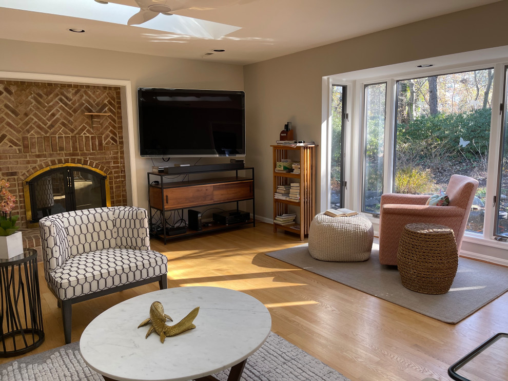 Immagine di un soggiorno minimal di medie dimensioni e aperto con pareti grigie, parquet chiaro, camino classico, cornice del camino in mattoni e TV autoportante