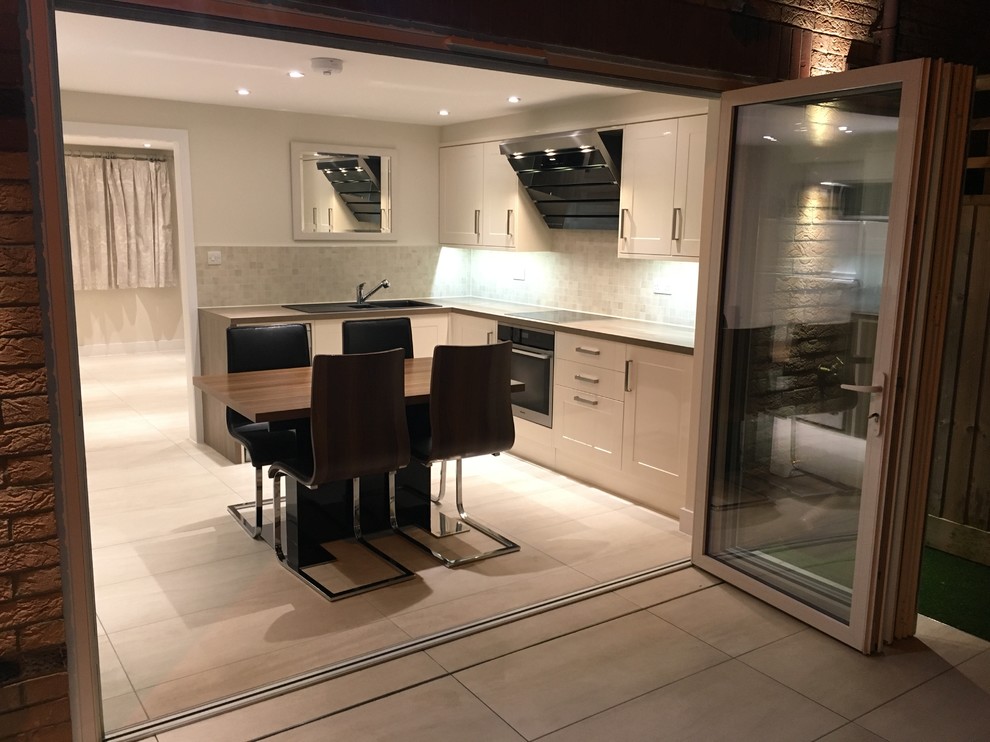 Small contemporary galley eat-in kitchen in Buckinghamshire with a single-bowl sink, flat-panel cabinets, beige cabinets, laminate benchtops, mosaic tile splashback, stainless steel appliances and ceramic floors.