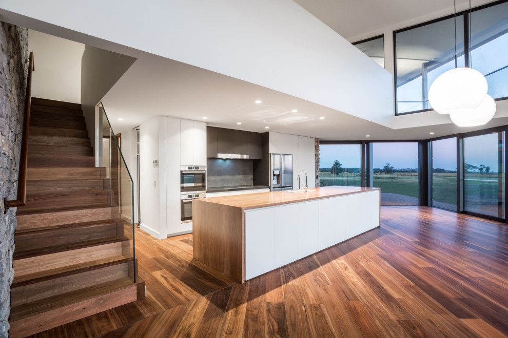 Large contemporary galley open plan kitchen in Melbourne with a drop-in sink, flat-panel cabinets, white cabinets, wood benchtops, grey splashback, porcelain splashback, stainless steel appliances, dark hardwood floors, with island, brown floor and brown benchtop.