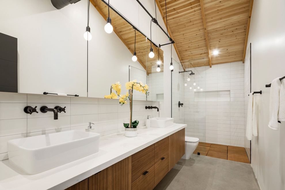 Inspiration for a mid-sized contemporary master bathroom in Phoenix with flat-panel cabinets, medium wood cabinets, a freestanding tub, a corner shower, white tile, ceramic tile, white walls, concrete floors, an undermount sink, solid surface benchtops, grey floor, a hinged shower door and white benchtops.