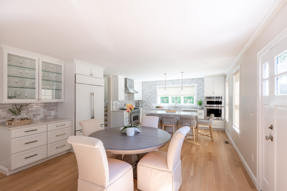 Example of a huge transitional l-shaped light wood floor and brown floor open concept kitchen design in Boston with an undermount sink, shaker cabinets, white cabinets, quartz countertops, gray backsplash, subway tile backsplash, stainless steel appliances, an island and white countertops