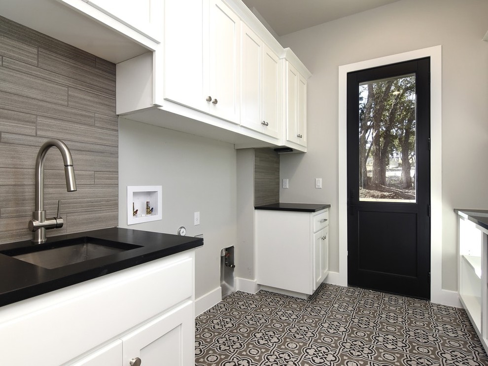 Mid-sized country galley dedicated laundry room in Austin with an undermount sink, shaker cabinets, white cabinets, solid surface benchtops, grey walls, porcelain floors, a side-by-side washer and dryer, grey floor and black benchtop.