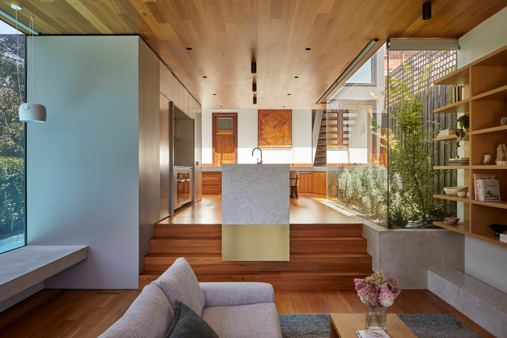 This is an example of a medium sized contemporary open plan living room in Melbourne with medium hardwood flooring, a timber clad ceiling, grey walls, a standard fireplace, a metal fireplace surround and a concealed tv.