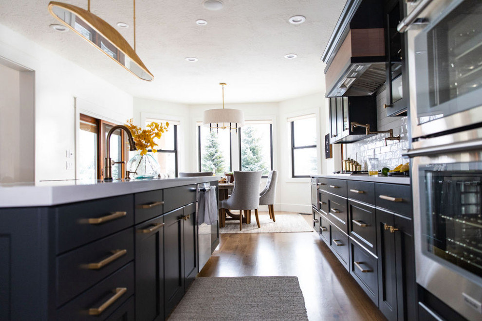 Example of a large transitional medium tone wood floor kitchen design in Seattle with an undermount sink, quartz countertops, white backsplash, subway tile backsplash, stainless steel appliances, an island and white countertops