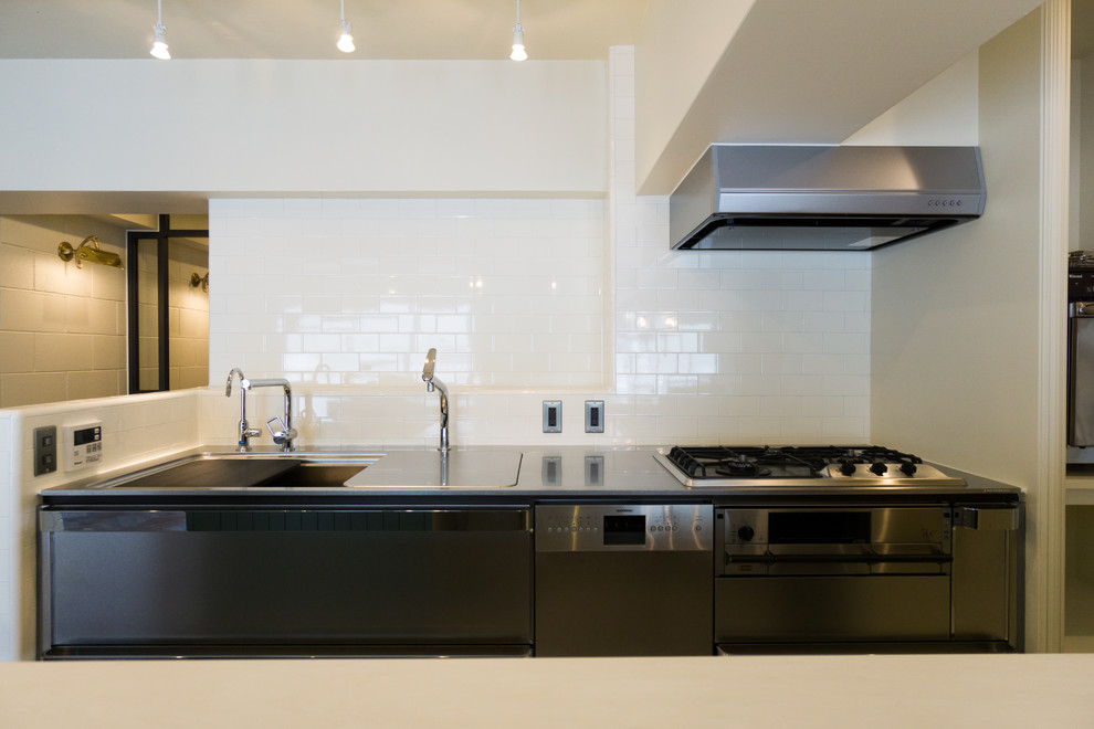 Industrial single-wall kitchen in Kobe with an integrated sink, white cabinets, solid surface benchtops, white splashback, porcelain splashback, stainless steel appliances, linoleum floors, with island and white floor.