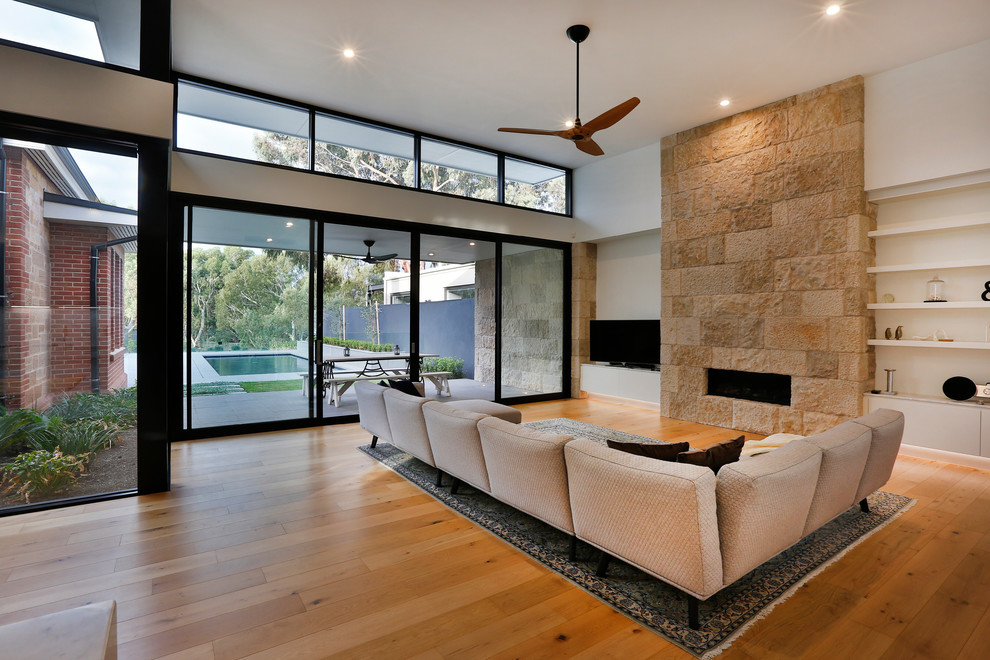 Large contemporary open concept living room in Adelaide with white walls, medium hardwood floors, a standard fireplace, a stone fireplace surround and a freestanding tv.