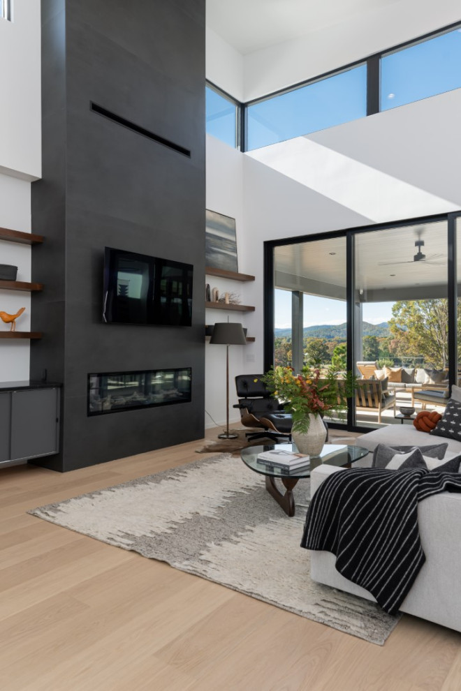 This is an example of a medium sized modern open plan living room in Other with white walls, light hardwood flooring, a standard fireplace, a tiled fireplace surround, a wall mounted tv, beige floors and a vaulted ceiling.