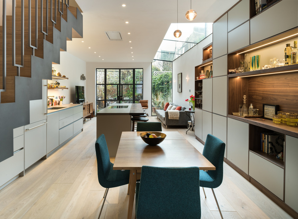 Design ideas for a large contemporary galley open plan kitchen in London with flat-panel cabinets, white cabinets, wood benchtops, brown splashback, timber splashback, light hardwood floors, with island, beige floor, brown benchtop and an undermount sink.