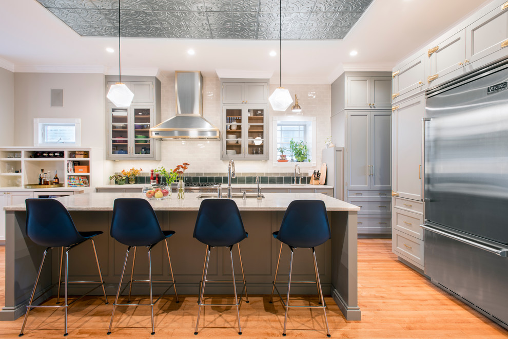 This is an example of a transitional kitchen in Chicago with an undermount sink, shaker cabinets, grey cabinets, white splashback, stainless steel appliances, light hardwood floors, with island, beige floor and subway tile splashback.