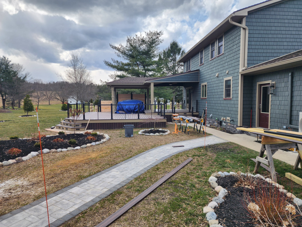 Photo of a large country backyard and ground level deck in New York with with privacy feature, a roof extension and cable railing.