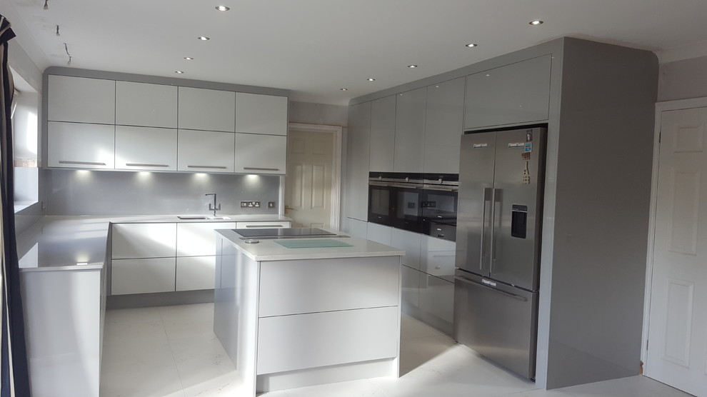 Photo of a large contemporary l-shaped open plan kitchen in Cambridgeshire with an integrated sink, flat-panel cabinets, grey cabinets, quartzite benchtops, grey splashback, panelled appliances, porcelain floors, with island and white floor.