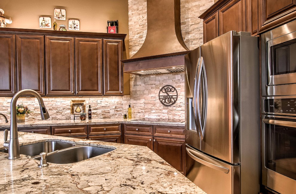 Large transitional l-shaped brown floor open concept kitchen photo in Phoenix with a double-bowl sink, raised-panel cabinets, dark wood cabinets, granite countertops, beige backsplash, stone tile backsplash, stainless steel appliances and an island