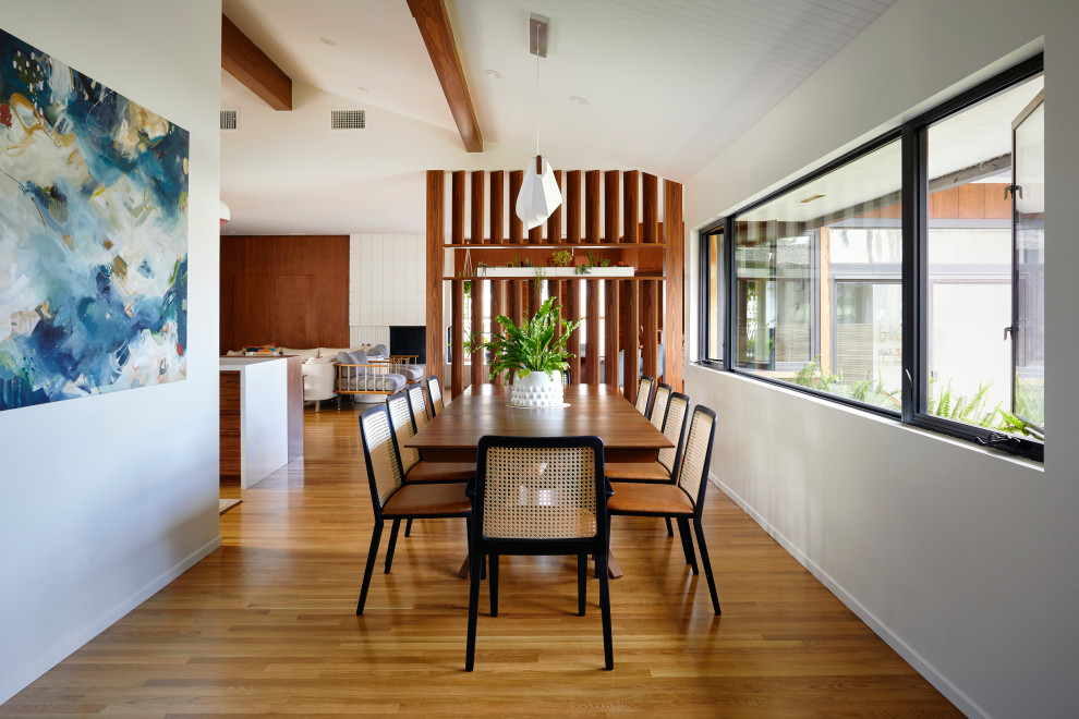 This is an example of a midcentury open plan dining in San Diego with white walls, light hardwood floors, a corner fireplace, a concrete fireplace surround and exposed beam.