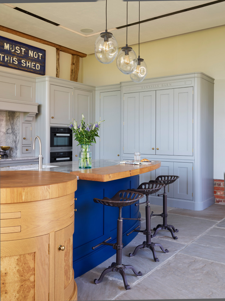 Inspiration for a country l-shaped eat-in kitchen in Essex with a farmhouse sink, shaker cabinets, grey cabinets, granite benchtops, grey splashback, granite splashback, black appliances, with island, grey floor and grey benchtop.