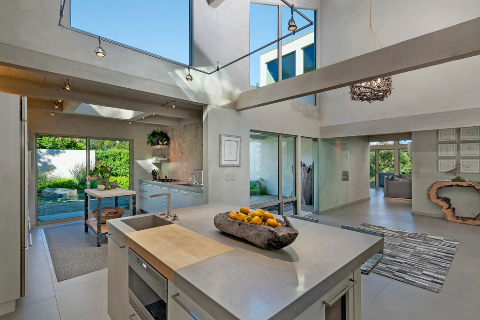 Photo of a large contemporary galley eat-in kitchen in Santa Barbara with an integrated sink, flat-panel cabinets, light wood cabinets, grey splashback, stone slab splashback, stainless steel appliances, multiple islands, solid surface benchtops and porcelain floors.