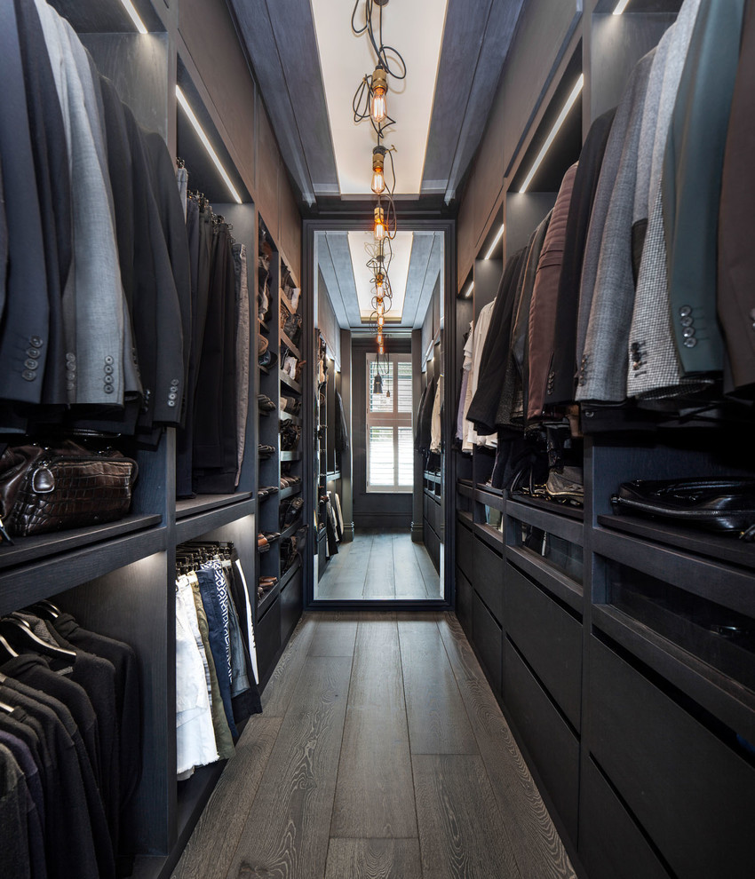 Mid-sized industrial men's storage and wardrobe in London with flat-panel cabinets, black cabinets, dark hardwood floors and brown floor.