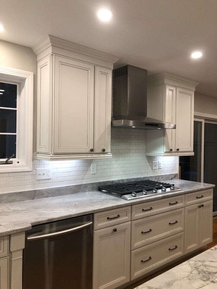 Large transitional l-shaped medium tone wood floor and brown floor open concept kitchen photo in Boston with an undermount sink, recessed-panel cabinets, white cabinets, quartz countertops, white backsplash, subway tile backsplash, stainless steel appliances, an island and multicolored countertops