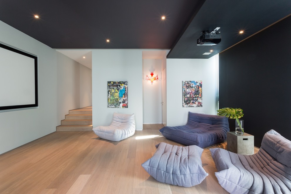 This is an example of a large contemporary enclosed home theatre in Miami with multi-coloured walls, light hardwood floors and a projector screen.