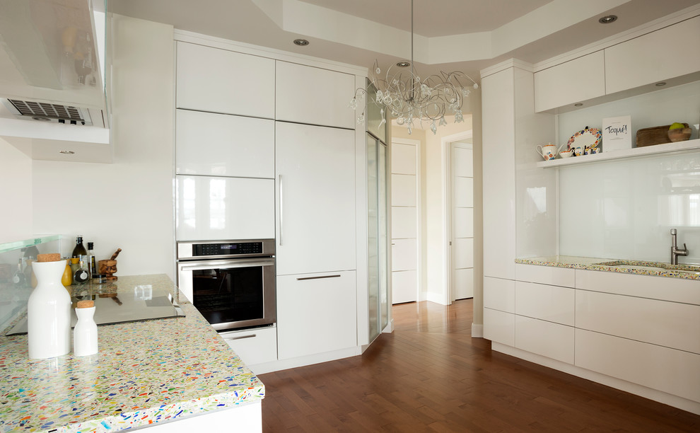 Photo of a mid-sized modern galley separate kitchen in Montreal with an undermount sink, flat-panel cabinets, white cabinets, recycled glass benchtops, white splashback, glass sheet splashback, white appliances, light hardwood floors and no island.