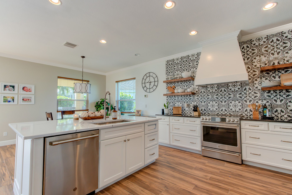 Example of a large transitional l-shaped ceramic tile and brown floor eat-in kitchen design with an undermount sink, shaker cabinets, white cabinets, quartz countertops, multicolored backsplash, ceramic backsplash, stainless steel appliances, an island and white countertops