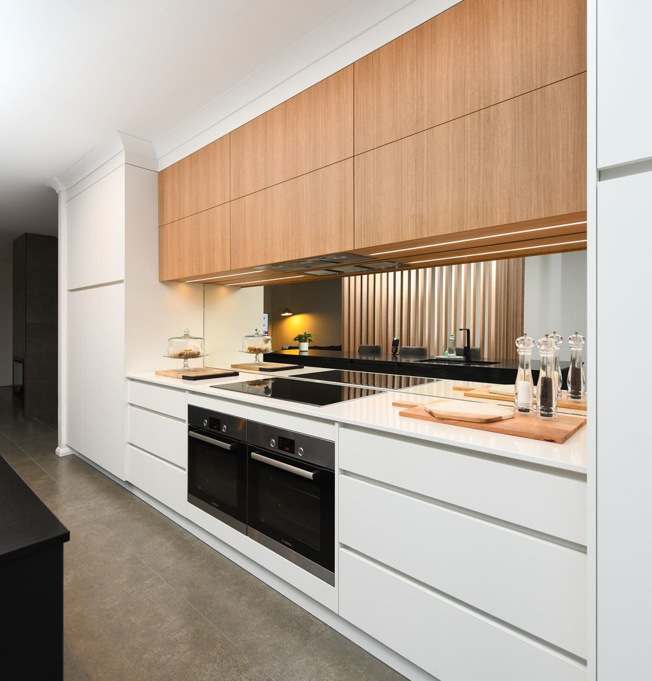 Inspiration for a modern galley eat-in kitchen in Other with a double-bowl sink, medium wood cabinets, limestone benchtops, mirror splashback, stainless steel appliances, cement tiles, with island, grey floor and black benchtop.
