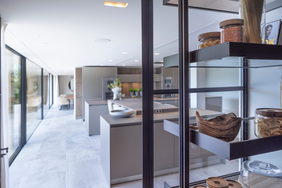 Large contemporary open plan kitchen in Cheshire with an integrated sink, flat-panel cabinets, medium wood cabinets, stainless steel benchtops, timber splashback, stainless steel appliances, ceramic floors, multiple islands, white floor and green benchtop.