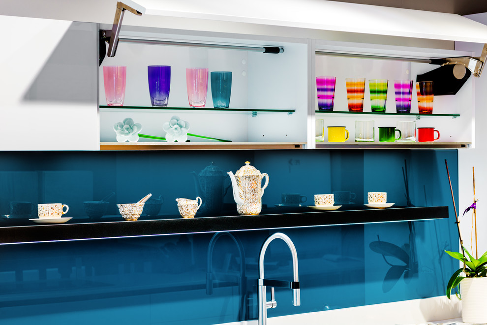 Large modern single-wall open plan kitchen in London with a drop-in sink, glass-front cabinets, white cabinets, quartzite benchtops, blue splashback, glass sheet splashback, panelled appliances, porcelain floors, a peninsula, grey floor and white benchtop.