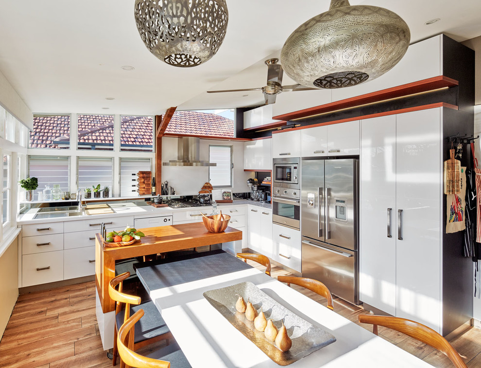 Inspiration for a contemporary l-shaped eat-in kitchen in Sydney with flat-panel cabinets, black splashback, stainless steel appliances, light hardwood floors and with island.