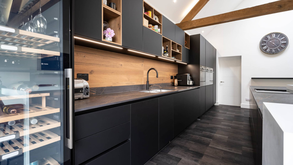 Design ideas for a mid-sized modern single-wall open plan kitchen in Oxfordshire with a double-bowl sink, flat-panel cabinets, black cabinets, quartzite benchtops, brown splashback, timber splashback, black appliances, with island, black floor, multi-coloured benchtop and exposed beam.