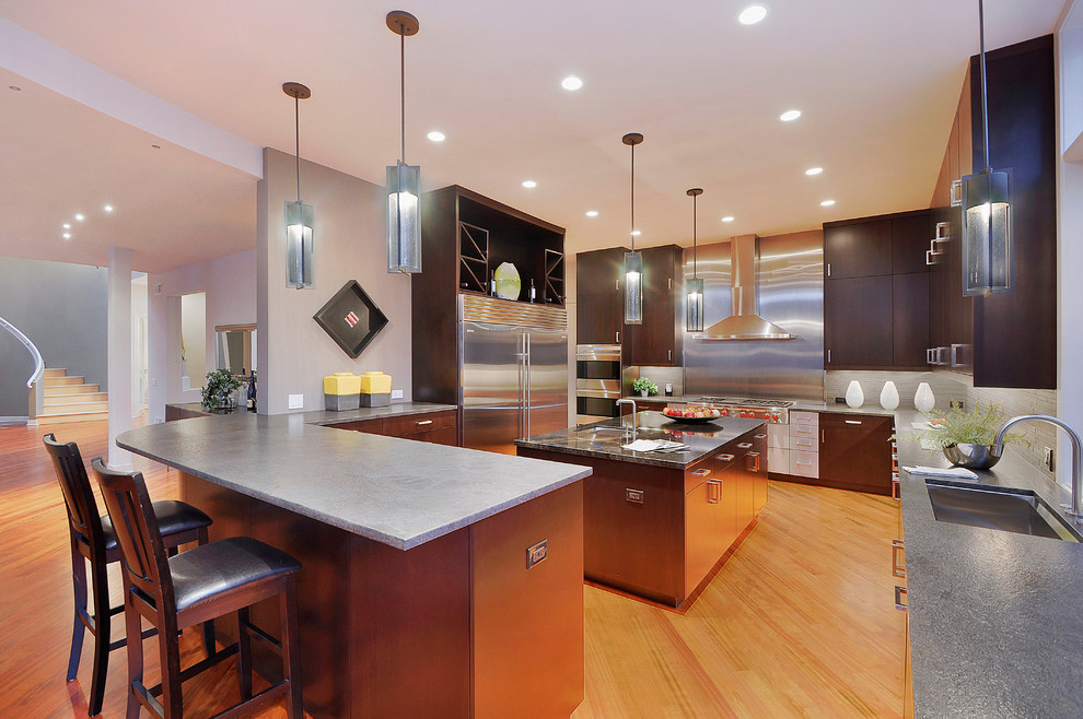 Photo of a large contemporary u-shaped eat-in kitchen in Chicago with an undermount sink, flat-panel cabinets, dark wood cabinets, concrete benchtops, grey splashback, matchstick tile splashback, stainless steel appliances, medium hardwood floors and with island.