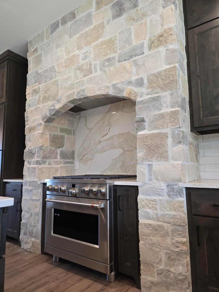 Large transitional brown floor kitchen photo with brown cabinets, quartz countertops, white backsplash, quartz backsplash, stainless steel appliances, an island and white countertops