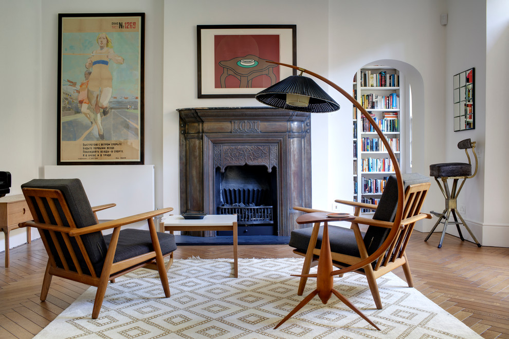 Photo of a mid-sized midcentury open concept living room in London with white walls, medium hardwood floors, a standard fireplace, a library, a metal fireplace surround and no tv.
