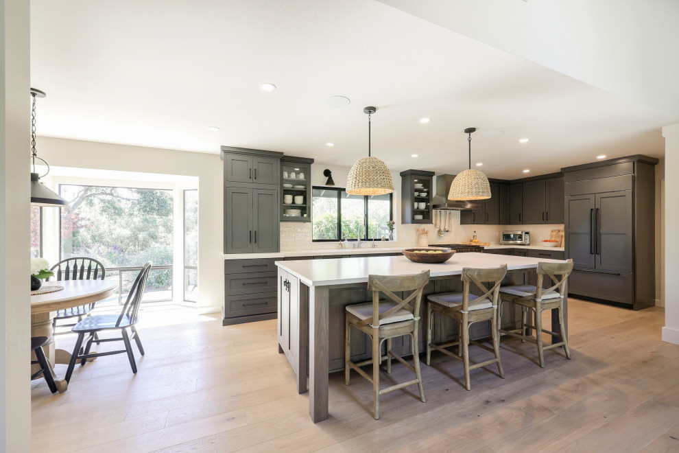 Example of a mid-sized transitional l-shaped laminate floor open concept kitchen design with a double-bowl sink, flat-panel cabinets, gray cabinets, quartz countertops, white backsplash, ceramic backsplash, stainless steel appliances, an island and white countertops