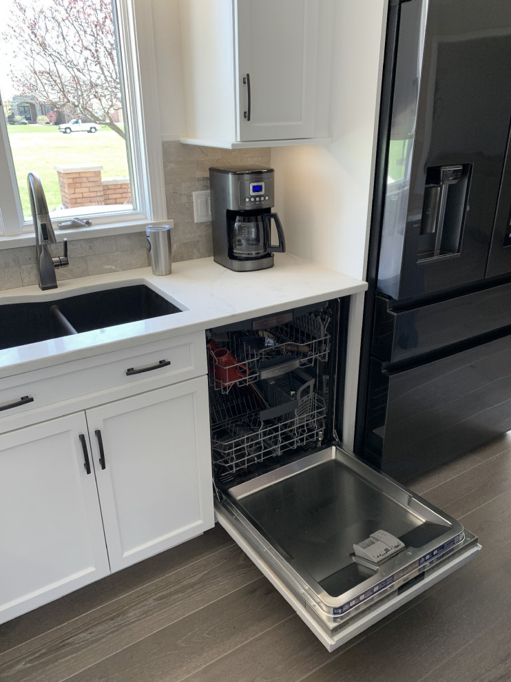 Example of a large transitional l-shaped vinyl floor and gray floor eat-in kitchen design with an undermount sink, recessed-panel cabinets, white cabinets, quartz countertops, gray backsplash, ceramic backsplash, stainless steel appliances, an island and white countertops