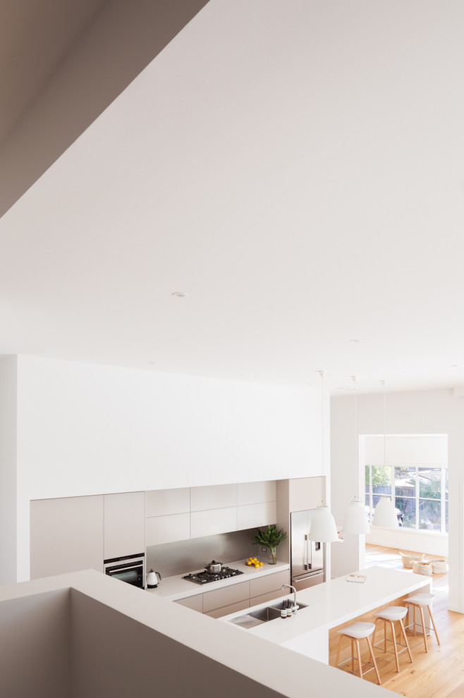 Inspiration for a mid-sized contemporary galley eat-in kitchen in Sydney with an undermount sink, flat-panel cabinets, beige cabinets, solid surface benchtops, grey splashback, stainless steel appliances, medium hardwood floors, with island, brown floor and porcelain splashback.