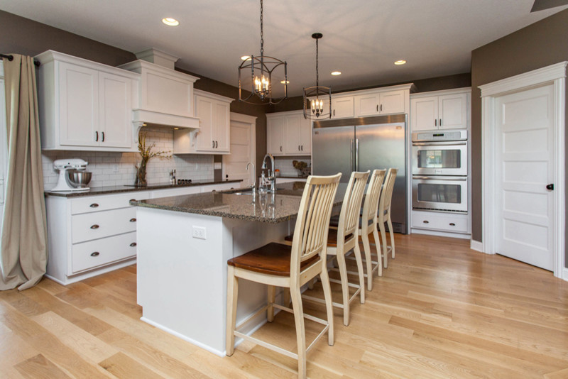 Mid-sized transitional l-shaped light wood floor open concept kitchen photo with an undermount sink, beaded inset cabinets, white cabinets, granite countertops, white backsplash, subway tile backsplash, stainless steel appliances and an island