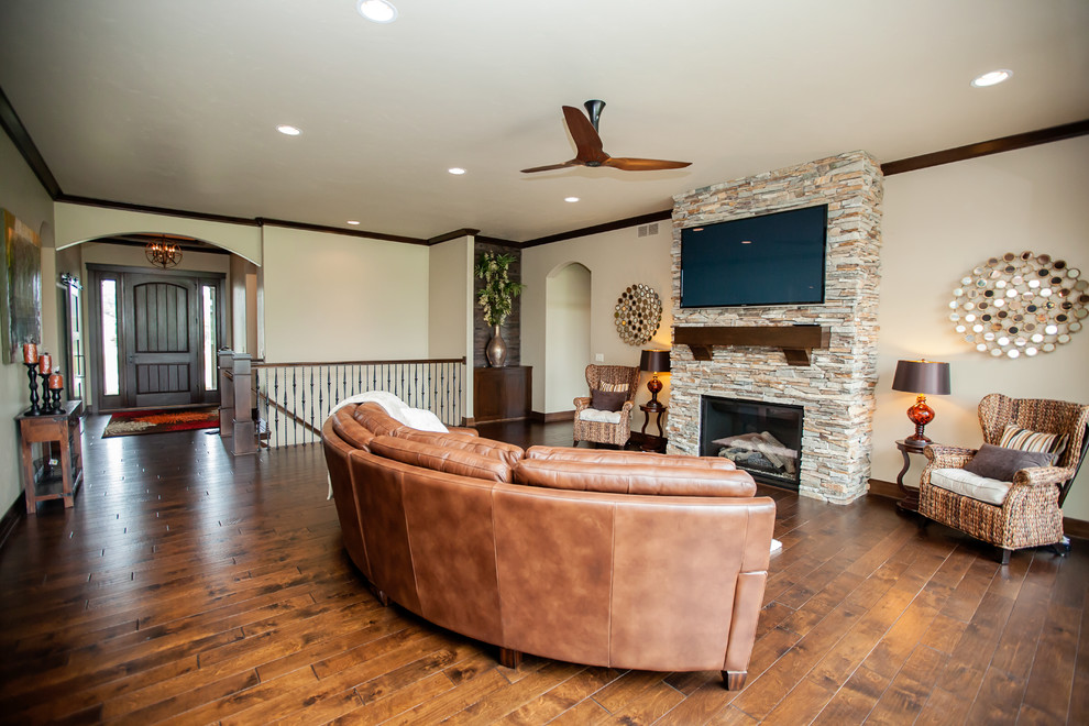 Large arts and crafts open concept living room in Milwaukee with medium hardwood floors, a standard fireplace, a stone fireplace surround, a wall-mounted tv and beige walls.