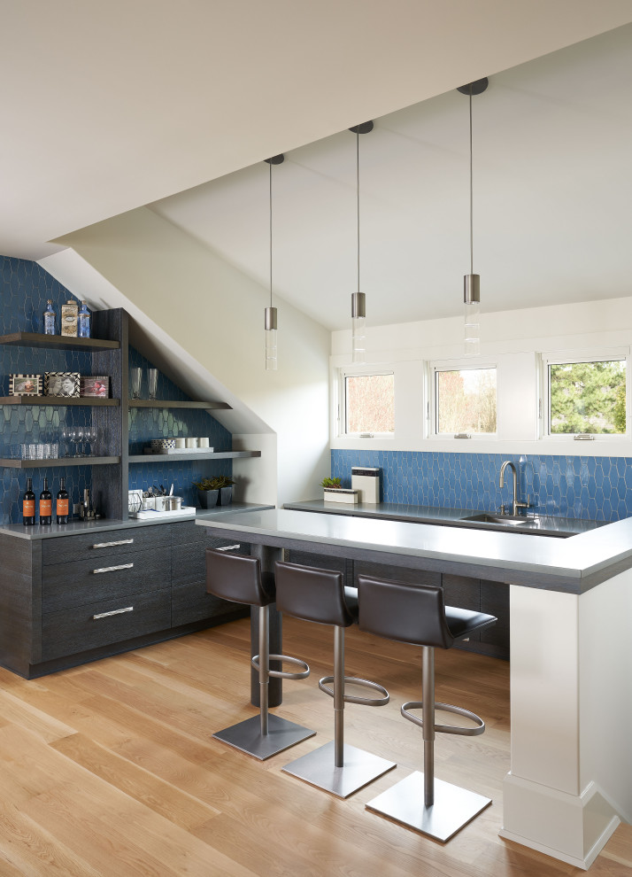 This is an example of a transitional l-shaped seated home bar in Houston with an undermount sink, flat-panel cabinets, grey cabinets, blue splashback, mosaic tile splashback, medium hardwood floors, brown floor and grey benchtop.