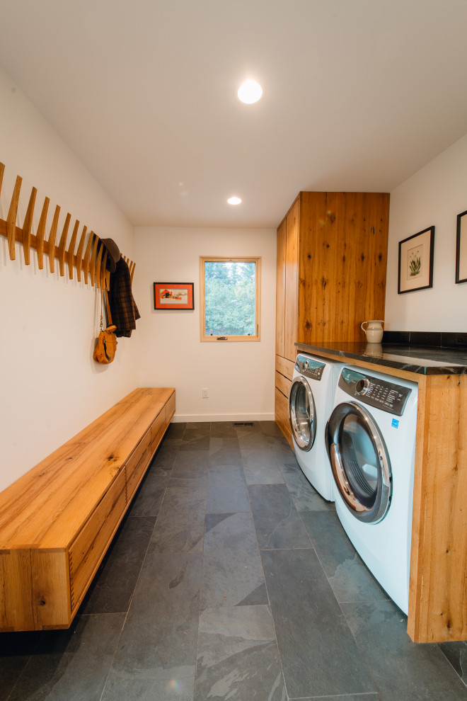 Photo of a large galley utility room in Denver with medium wood cabinets, white walls, ceramic floors, a side-by-side washer and dryer, black floor and black benchtop.