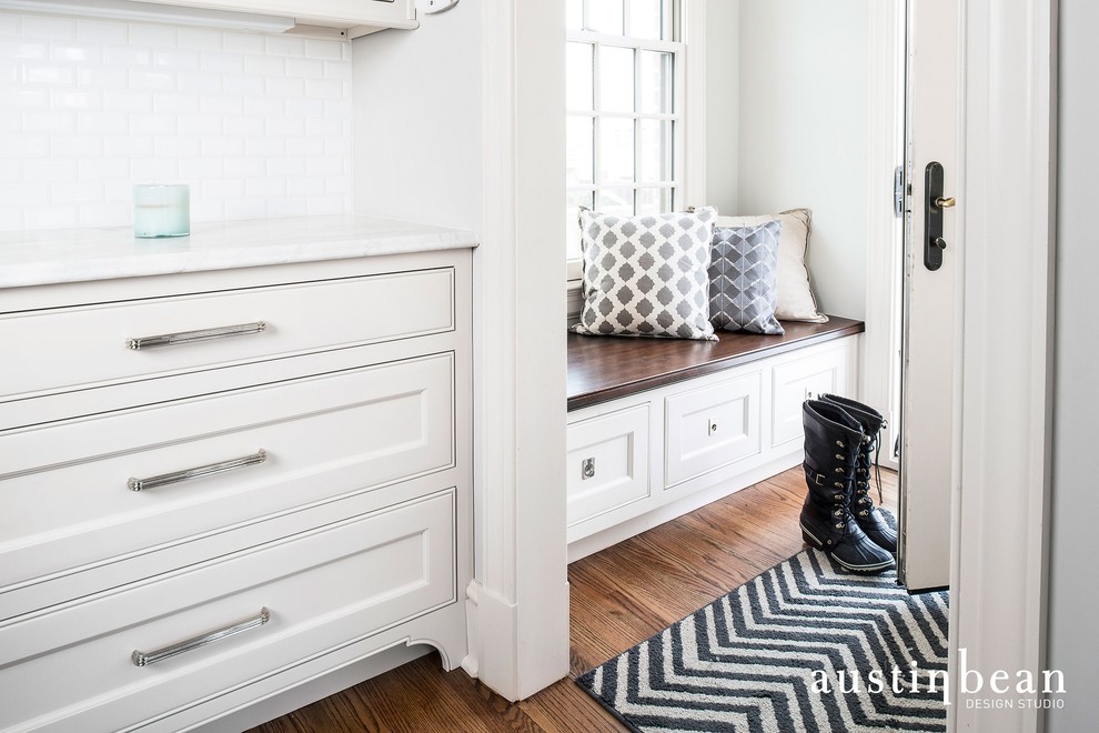 Transitional medium tone wood floor kitchen photo with a farmhouse sink, glass-front cabinets, white cabinets, marble countertops, white backsplash, subway tile backsplash, stainless steel appliances and gray walls