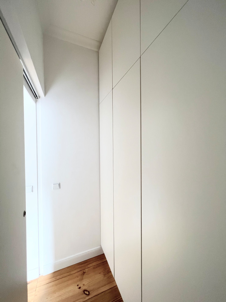 Immagine di un piccolo ripostiglio-lavanderia minimal con ante lisce, ante bianche, pareti bianche, parquet chiaro e pavimento marrone