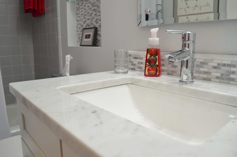 Example of a transitional gray tile bathroom design with an undermount sink, shaker cabinets, white cabinets and marble countertops